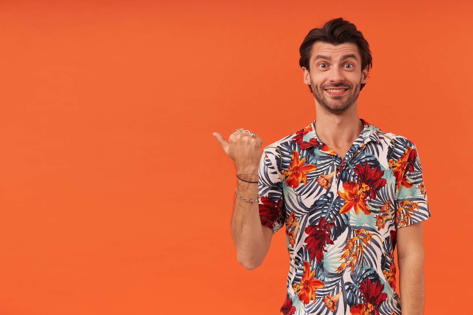 happy-attractive-young-man-with-bristle-hawaiian-shirt-pointing-side-copyspace-by-thumb-finger
